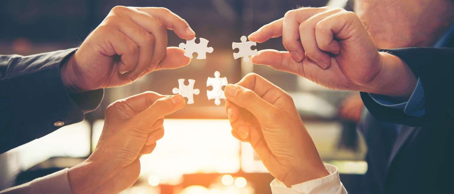 Four people bringing puzzle pieces together in a workshop