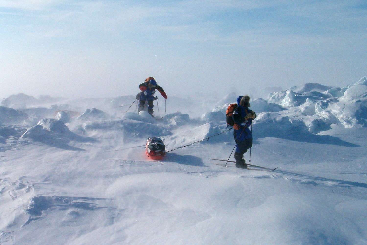 Arctic explorers skiing across ice, towing a sled in high wind