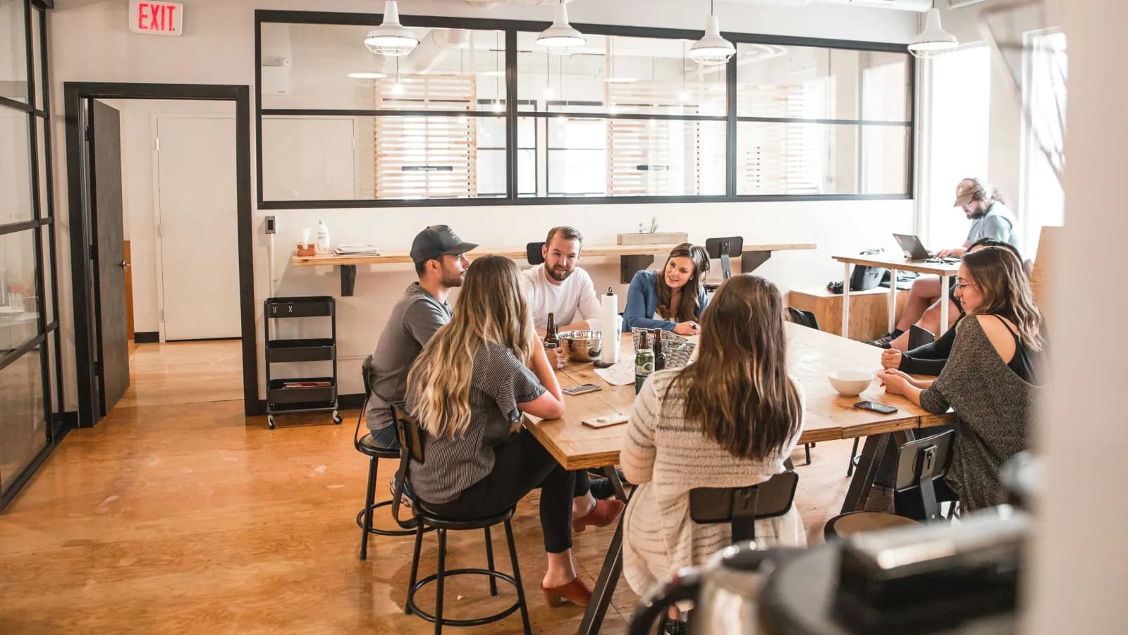 How do you make communication consistent across sales and service teams?. Colleagues talking around a long table in an open-plan office