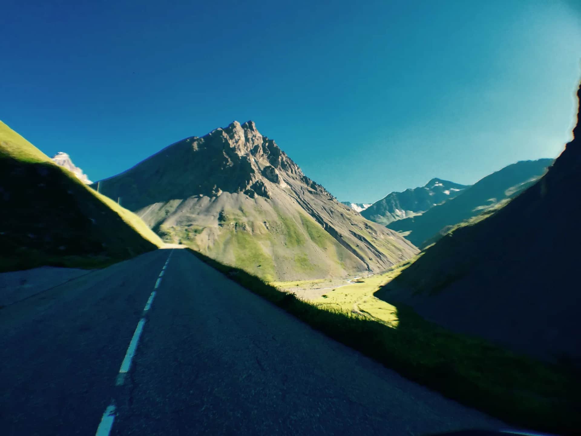 An empty mountain road curving toward a rocky alpine peak