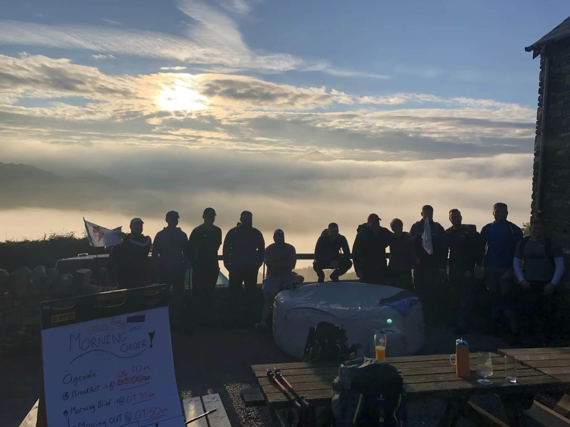 A group silhouetted on a mountain terrace above a sea of cloud at sunrise