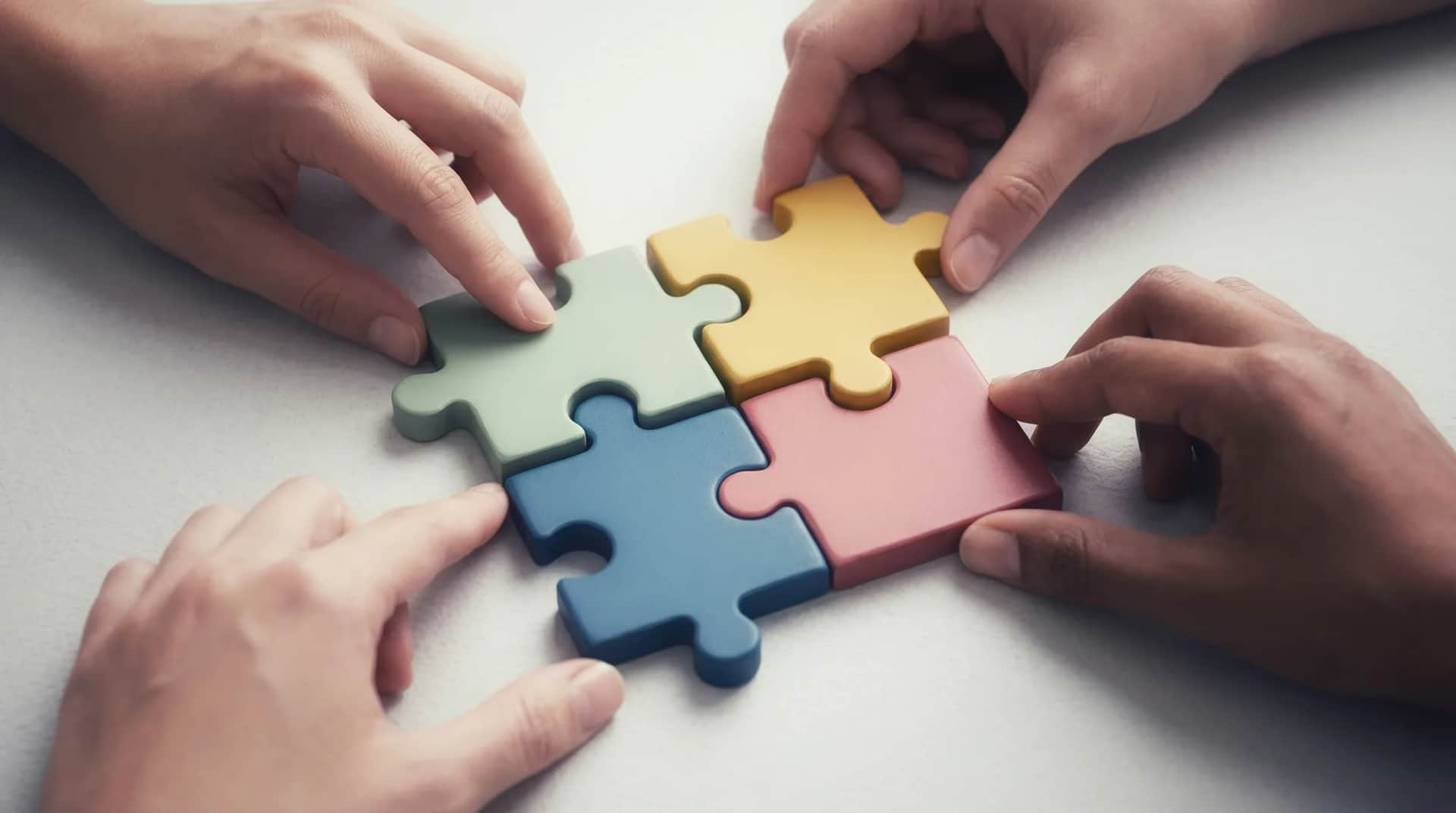 Four hands sliding four jigsaw pieces together into a single square
