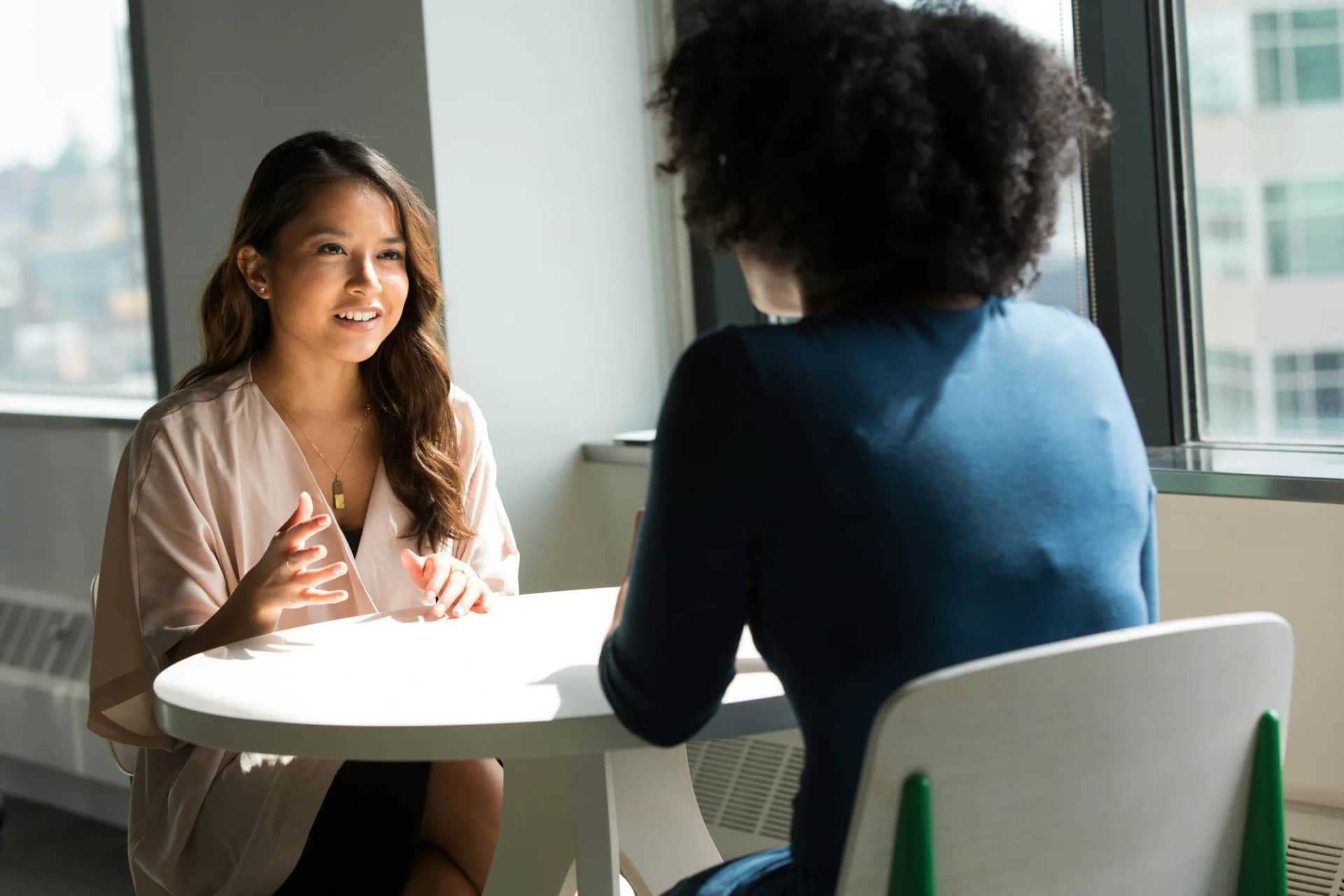 How do you shift a leadership culture from performance management to coaching and empowerment?. Two colleagues talking across a small table by a window