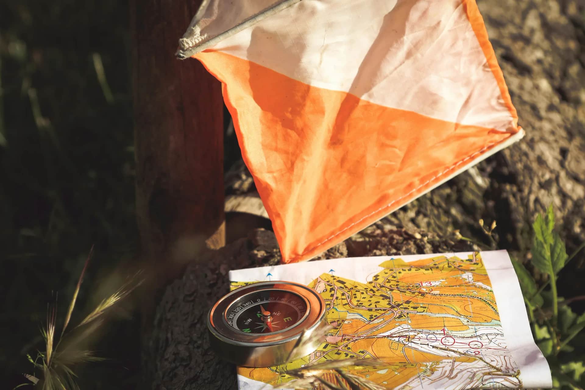 An orienteering control flag, a compass and a map spread on a tree stump in woodland
