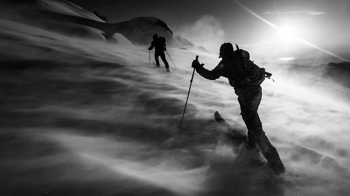 Two ski tourers pushing uphill through blowing snow in a whiteout