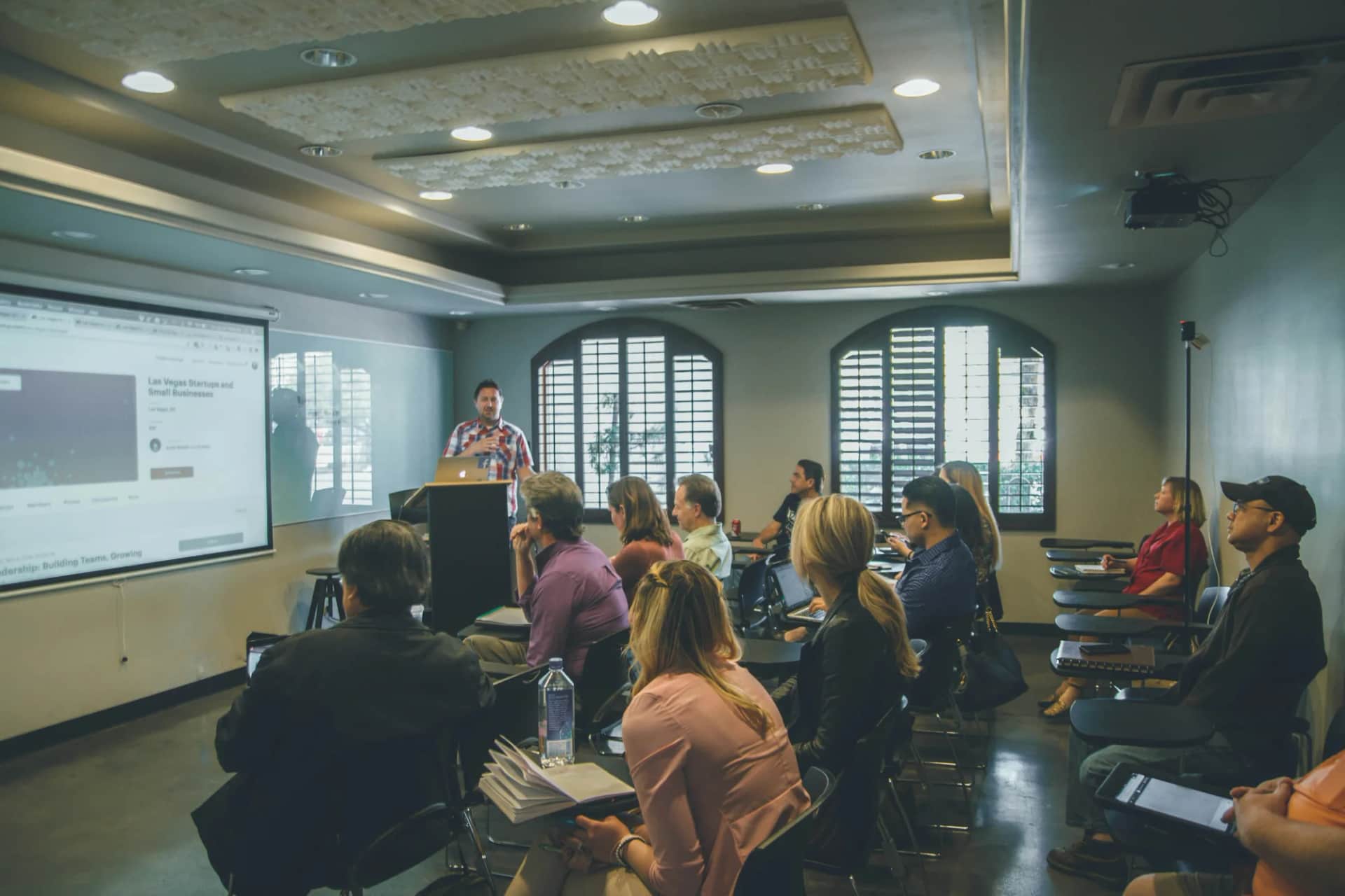 How do you bring company values to life for a senior executive board?. A speaker at a lectern addressing a seated audience, a screen behind them