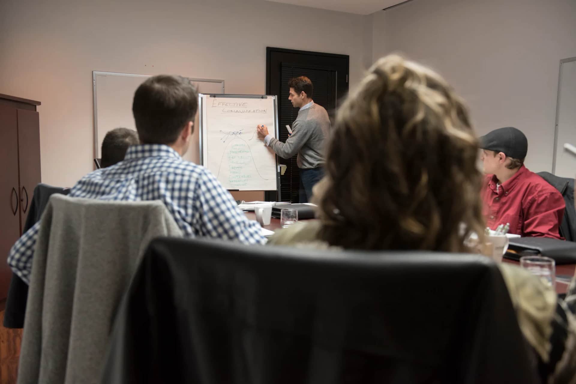 How do you design a high-impact graduate programme for a global cohort?. A facilitator writing on a flipchart for a small group seated around a table