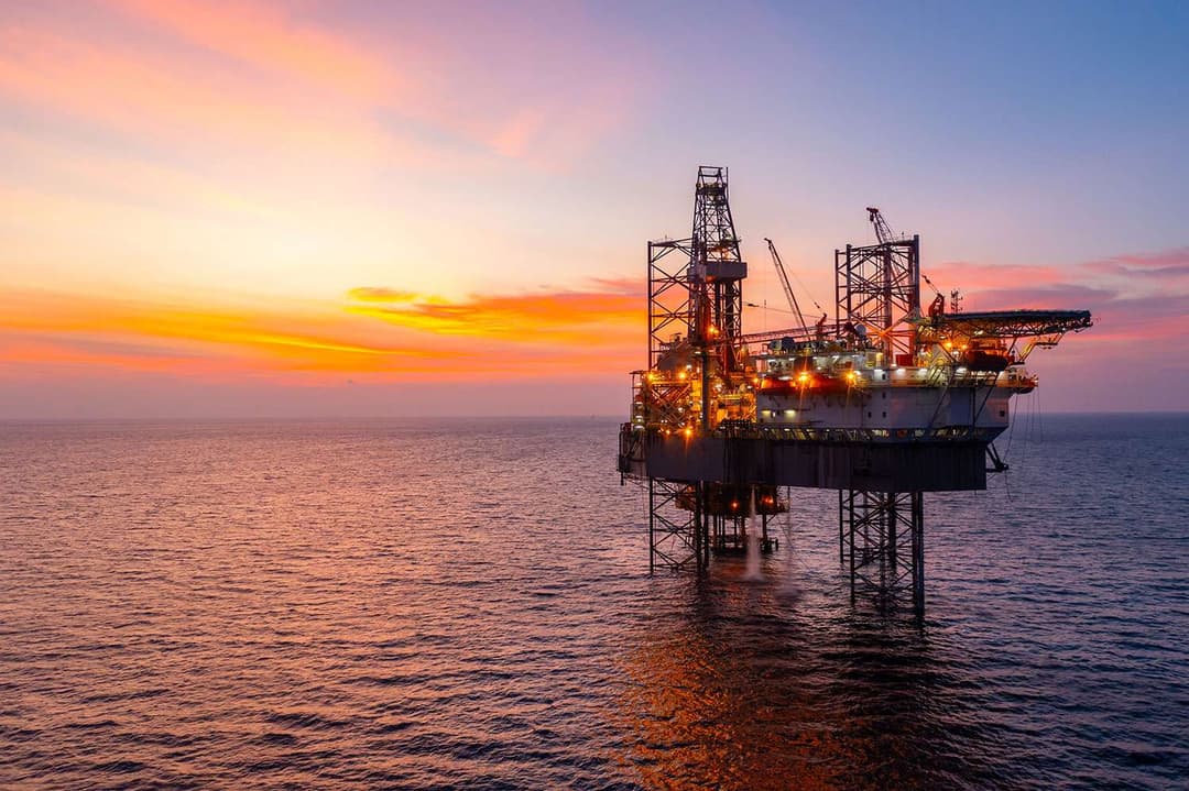 Oil rig in the ocean with sunsetting behind it